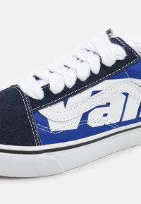 Tumed sinine toss, millel on valged nöörid ja suur valge Vans'i logo. Valmistatud nahast ja kanvasest, kontrastsete õmblustega ning musta tallaga.