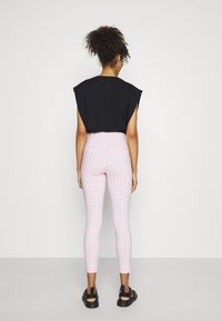Top negro sin mangas, pantalones de cuadros rosas de cintura alta, ajustados y de largo hasta el tobillo. El calzado tiene tiras negras y una suela gruesa.