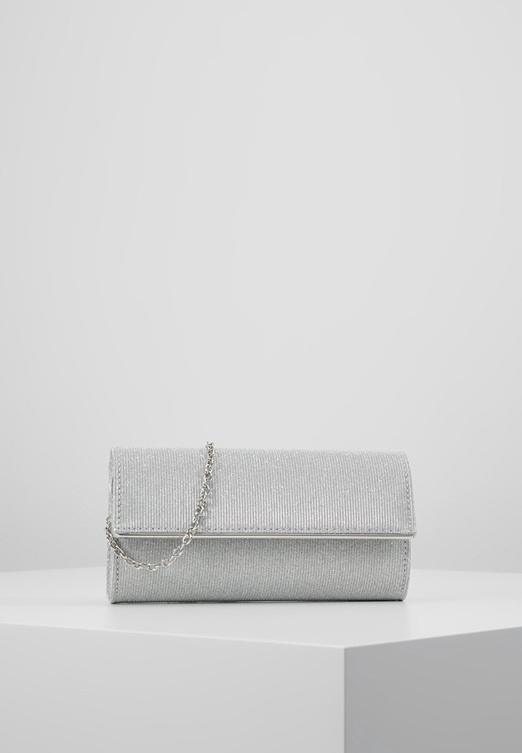 Pochette pailletée argentée avec rabat et fine chaîne argentée, présentée sur un piédestal blanc devant un fond gris clair.