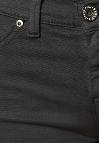 Svarta denimjeans med en mjuk yta, med en silverknapp och en liten fickdetalj. Fokus på midjebandet och sömmarna.