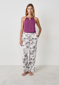 Camisola viola con spalline sottili abbinata a pantaloni larghi bianchi con stampa tropicale di foglie nere e rosa e tasche.