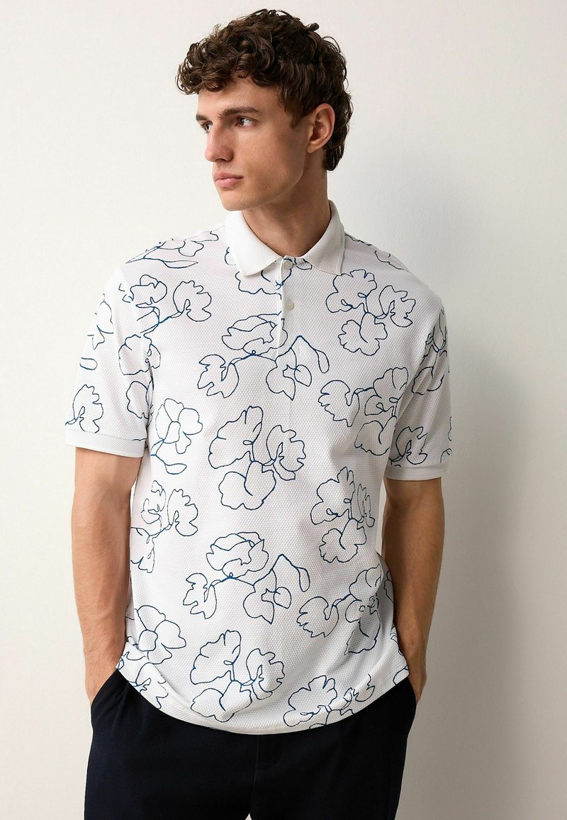 Tricou polo alb cu un model texturat, având contururi florale albastre. Mâneci scurte și guler cu două butoane.