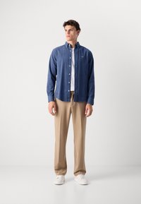 Marine geknopt overhemd, katoenen stof, lange mouwen, borstlogo, gecombineerd met beige broek en witte sneakers. Schoon, op maat gemaakt pasvorm.