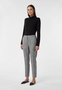 Zwarte langemouwen coltrui, grijze geblokte broek met een getailleerde pasvorm en vlakke voorkant, gecombineerd met zwarte puntige ballerina's. Eenvoudige accessoires.
