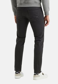 Jeans ajustados de color gris oscuro, fabricados en algodón, con bolsillos traseros y detalles de costura sutiles, llevados con zapatillas blancas que presentan un logotipo de marca.