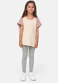 Kremfarget t-skjorte med beige skulderdetaljer, sammen med grå leggings og hvite sneakers. Glatt tekstur, avslappet passform.