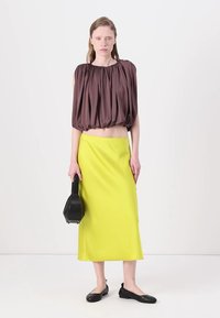 Brown, pleated short-sleeve top; bright yellow, ankle-length skirt; black flat shoes; small black handbag. Simple and modern design.