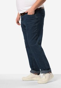 Jeans de mezclilla azul oscuro con un diseño de pierna recta, que presentan un estilo clásico de cinco bolsillos y puños enrollados. Combinados con zapatillas blancas.