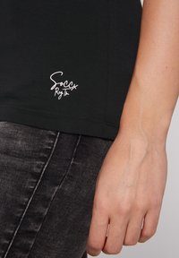 Camiseta de algodón negra con logo impreso en blanco "Soccx Reg Tn" en el dobladillo inferior, con un corte ajustado y mangas cortas.