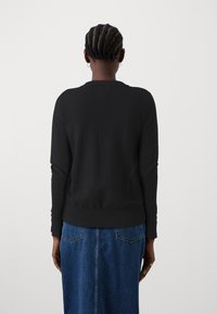 Zwarte gebreide trui met een ronde hals, ribgebreide manchetten en zoom. Gedragen over een denim rok, die een gladde textuur en een aansluitend ontwerp toont.