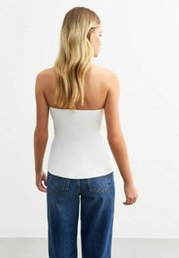 Vit, axelbandslös topp med en åtsittande design och slät textur, kombinerad med högmidjade blå denimjeans, sedd bakifrån.