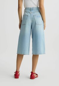 Culotte din denim de culoare bleu deschis, cu talie medie, având două buzunare pe spate și tiv finisat. Asortate cu sandale roșii cu curele.