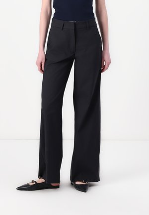 Wide-leg black trousers made from smooth fabric, featuring a flat front, side pockets, a tailored fit, and paired with pointed black flats.