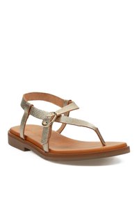 Sandalias planas doradas con un diseño de tiras texturizadas y una hebilla circular decorativa, colocadas sobre una suela marrón claro, que exhiben un estilo veraniego elegante.
