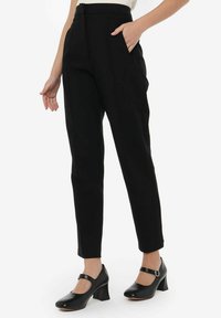 Pantalones negros ajustados con bolsillos laterales, cintura alta y diseño de pierna recta. La tela parece suave y ligeramente estructurada.