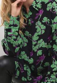 Camisa negra con un estampado floral que incluye hojas verdes y acentos morados. Confeccionada en una tela suave, cuenta con cierres de botón y cuello.