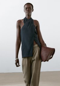 Námořnický halter top z lehké látky, doplněný světle hnědými pruhovanými kalhotami. Modelka drží pletenou vínově červenou kabelku.