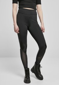Juodos sportinės legging'os su lygiu paviršiumi ir tinklinėmis akcentais, turinčios aukštą juosmenį ir geometrinį panele dizainą. Suderintos su juodais karybiniais batais.