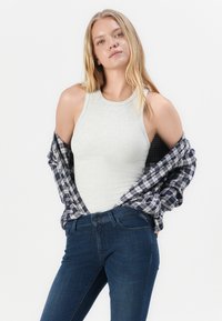 Világosszürke bordázott ujjatlan felső egy kék kockás flaneling alatt, sötétkék, testhezálló farmerral párosítva. Egyszerű, hétköznapi stílus.