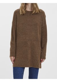 Brązowy, oversize'owy sweter wykonany z miękkiego, teksturowanego materiału; z okrągłym dekoltem i długimi rękawami, zestawiony z niebieskimi dżinsami.