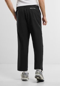 Pantaloni negri din bumbac cu talie elastică, buzunare laterale și logo alb brodat pe spate. Au un design cu picior drept.