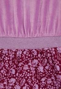 Fialová a burgundská tkanina s textúrovaným vrchom s vertikálnymi ryhami a spodnou časťou s kvetinovým vzorom, oddelené jednofarebným pásom.