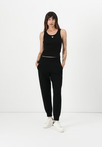Svart, kort tanktopp med trekantet detalj, sammen med svarte joggebukser med sidelommer og elastiske mansjetter, båret med hvite joggesko.