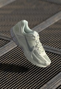 Svijetlozeleni Nike trkači tenisice s mrežastim dizajnom i sivoj swoosh logotipu počiva na metalnoj rešetkastoj površini.