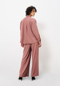 Rosa metallisches Loungewear-Set bestehend aus einem entspannten Langarmoberteil und weiteren Hosen mit weitem Bein. Weicher Stoff mit einem subtilen Glanz. High Heels.