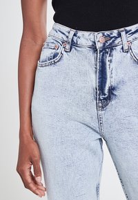 Jeans en denim bleu clair avec un design à cinq poches, taille haute, détails usés et quincaillerie en cuivre. Silhouette ajustée avec un minimum d'élasticité.