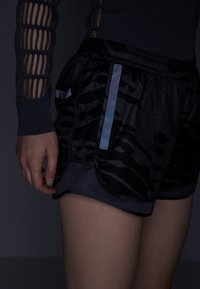 Svarta sportshorts med tigerstrimmönster, meshinserts på sidorna och iriserande detaljer. Har resårmidja och fickor.