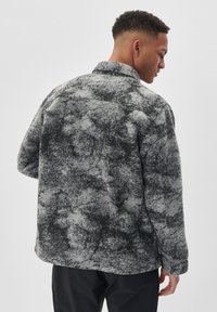 Jachetă din fleece cu model gri și negru, cu guler și mâneci lungi, având o croială lejeră și un material texturat.