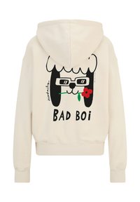 Crèmefarbener Kapuzenpullover mit einem Aufdruck eines Cartoon-Hundes, der eine Brille trägt und eine Blume hält, sowie dem Text "BAD BOI" in fetten schwarzen Buchstaben.