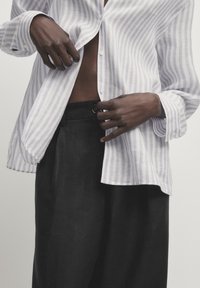 Randig skjorta i ljuslila och vitt, med avslappnad passform och långa ärmar, parat med mörka, strukturerade byxor med hög midja.