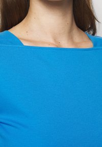 Blå mössa med ribbat mönster, bred fyrkantig halsringning, slät textur och figurnära passform, designad för att sitta tight mot kroppen.