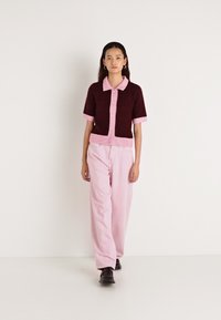 Bordo ar īsām piedurknēm kardigans ar rozā apkakli un pogām, kopā ar gaismas rozā vaļīgām biksēm. Modelis valkā melnus apavus.