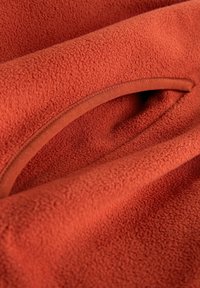 Terrakotta gyapjúszövet puha, texturált felülettel; a szélén sima, lekerekített kivágásos mintával.