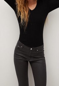 Top negro de manga larga con canesú en V y diseño ajustado, combinado con pantalones de mezclilla gris oscuro que presentan detalles de herrajes sutiles.
