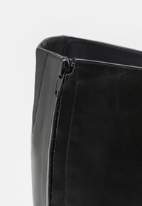 Čierna kožená čižma s hladkou textúrou, rovnou siluetou a bočným zipsom s brandingom YKK pre jednoduchý prístup.