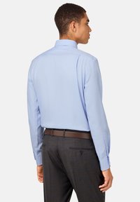 Camicia azzurra a maniche lunghe con colletto standard, abbinata a pantaloni grigio ardesia e una cintura marrone. Tessuto con una leggera texture sulla camicia.