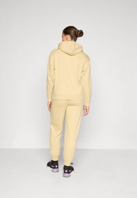 Beige hoodie och matchande joggers gjorda av mjukt tyg, med avslappnad passform och ribbade cuffs. Svarta sneakers med rosa detaljer fulländar looken.