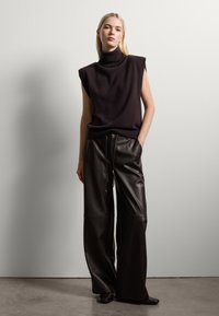 Un pull sans manches brun foncé à col roulé associé à un pantalon en cuir taille haute à jambes larges, doté d'une taille à cordon et d'une texture lisse.