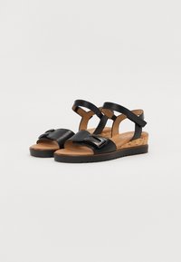 Black leather wedge sandals with a cork sole, featuring an adjustable ankle strap, wide front band, and silver-tone buckle detail.