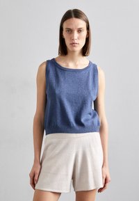 Blå ermeløs topp i mykt strikket stoff, med rund halslinning og avslappet passform. Kombinert med lyse beige, teksturerte shorts med bred midjebånd.