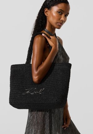 Čierna tkaná taška s uchom s textúrovaným háčkovaným dizajnom a podpisovým logom "Karl" v striebre na prednej strane, s pletenými rúčkami.