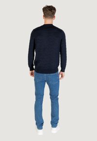 Marineblauer Pullover mit Wellenmuster, kombiniert mit hellblauen Jeans und weißen Sneakers. Sicht von hinten, die Passform des Outfits demonstrierend.