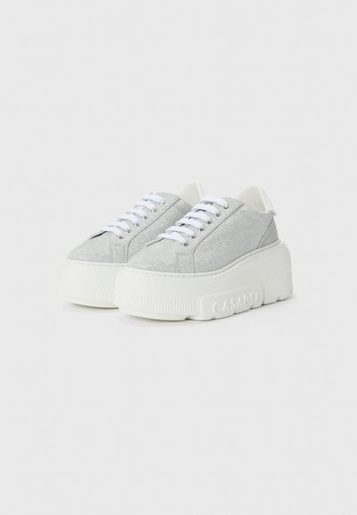 Silver fabric sneakers with a chunky white rubber sole, featuring white laces and subtle branding on the side. Smooth, textured surface.