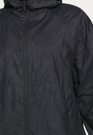 Veste en tissu noir froissé avec fermeture éclair à l'avant, col montant et poche zippée sur le côté, vue de la poitrine à la taille.