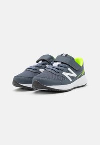 Baskets de sport grises avec tige en mesh, détails blancs et accents vert néon. Équipées d'une sangle Velcro et d'une semelle extérieure en caoutchouc texturé.