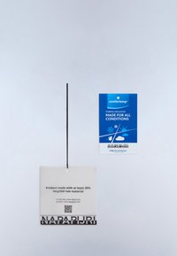 Dwie metki odzieżowe, jedna biała z tekstem o materiałach z recyklingu i kodem QR, druga niebieska reklamująca izolację termiczną na każdą pogodę.